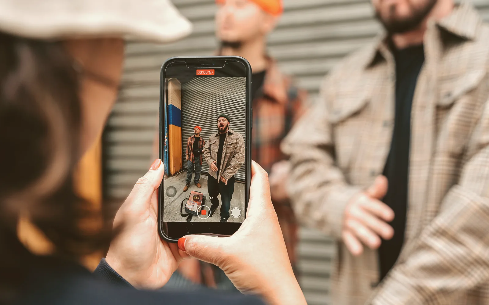 A worker in work clothes holds a phone in both hands, filming a coworker who points at the finished job in late afternoon light.