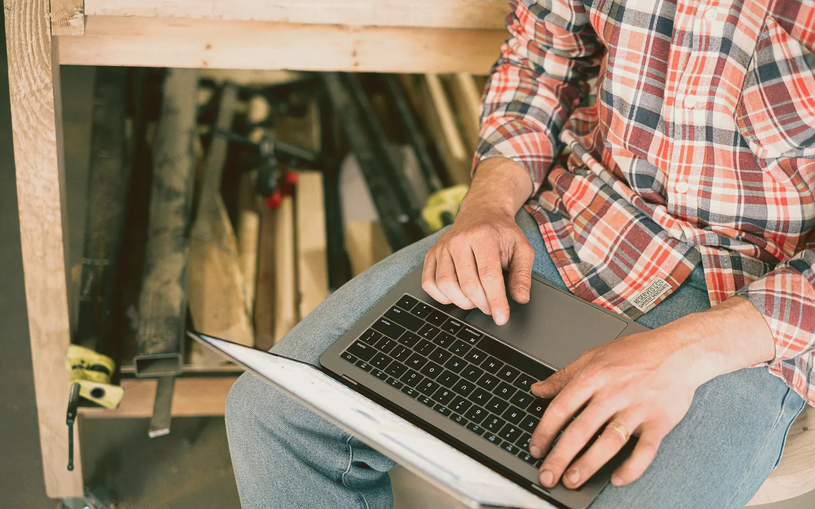 Two people in a small contractor office lean over a laptop while one holds a printed sheet of numbers