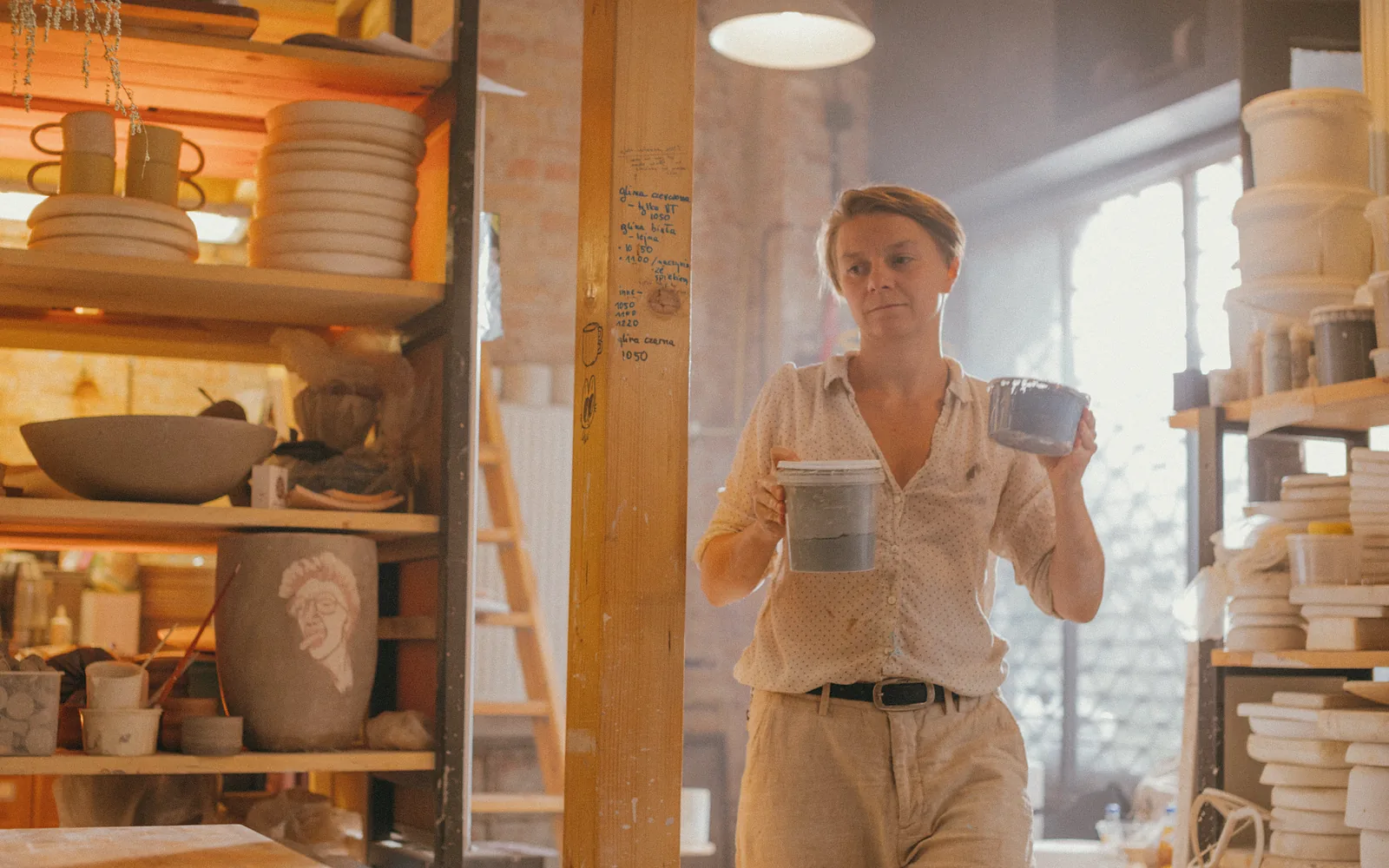 A potter crosses her workshop past shelves filled with everything she has already made