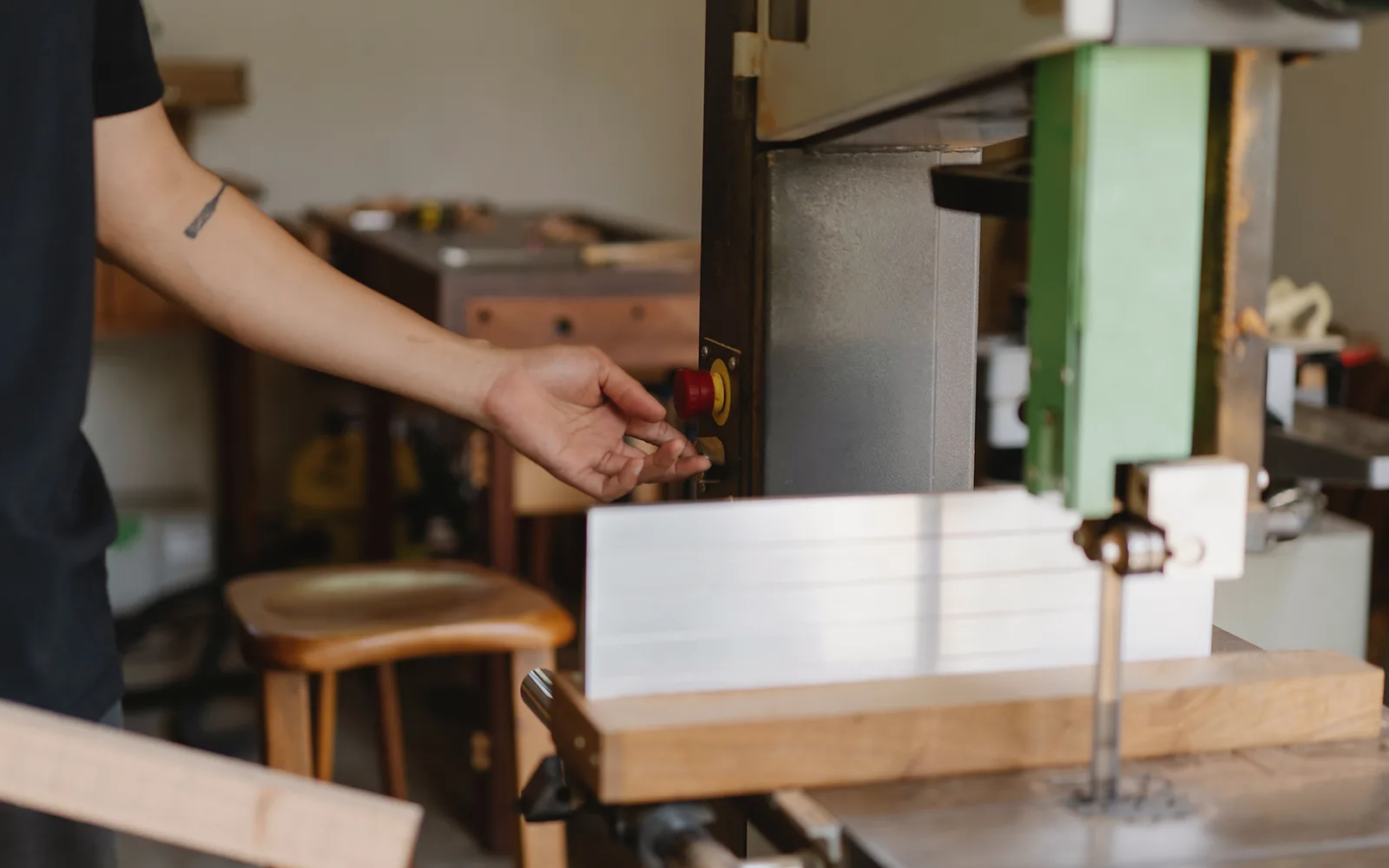 A hand reaches for the start button of the band saw in her own workshop
